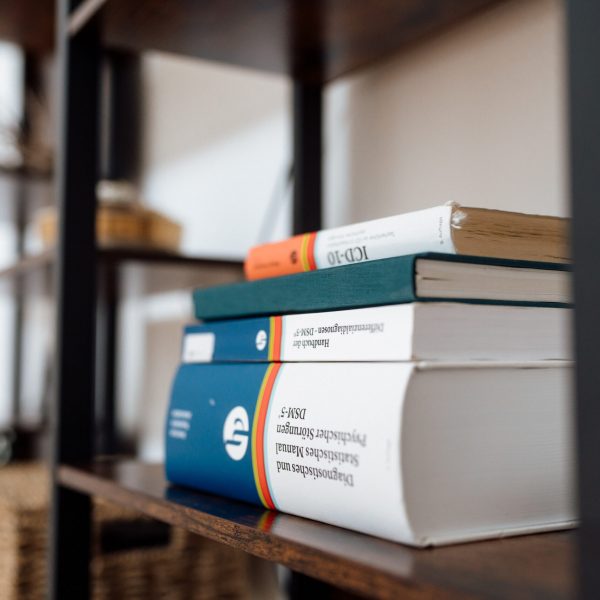 Diagnostikbücher in einem Schrank darunter Titel wie 'DSM-5' 'Handbuch der Differentialdiagnostik' und 'ICD-10'.
